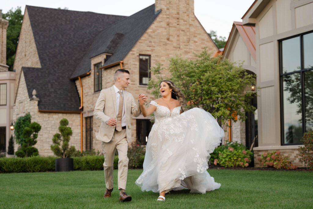 a happy bride and groom run through the grass at Venue3Two towards their Grand Rapids wedding photographer