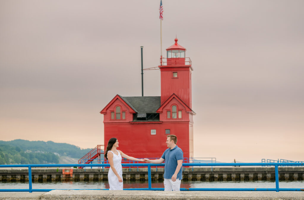 a engaged couple in front of the red lighthouse at Holland State Park