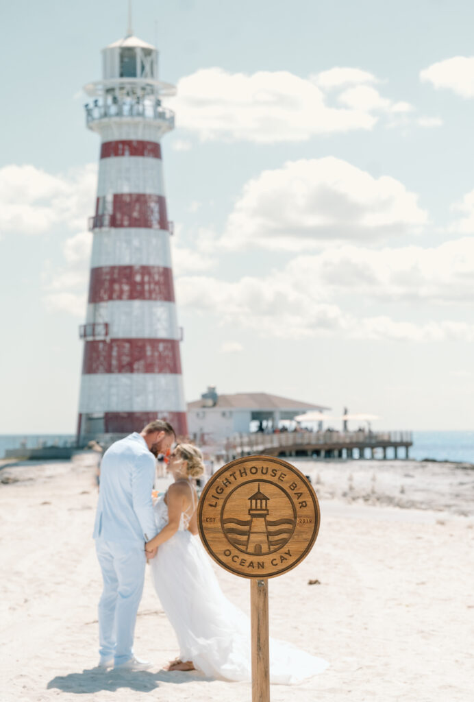 A bride and groom kiss in front of a light house at a port on their cruise wedding trip