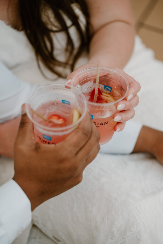 A bride and groom says cheers with their drinks on their wedding cruise ship